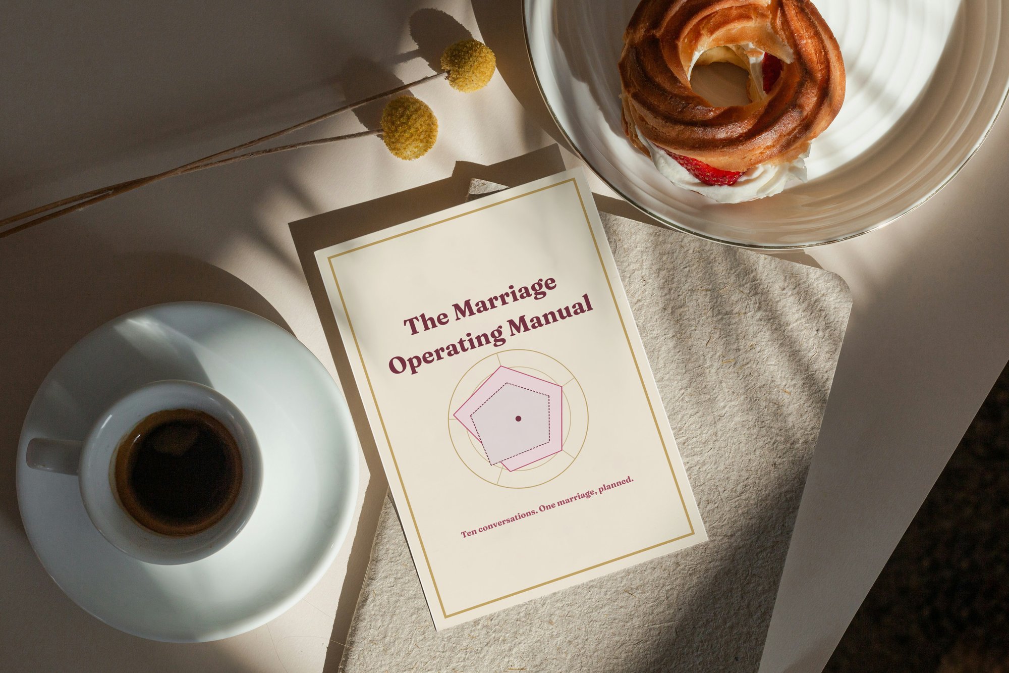 The Marriage Operating Manual guide resting on a linen table beside a coffee and a pastry
